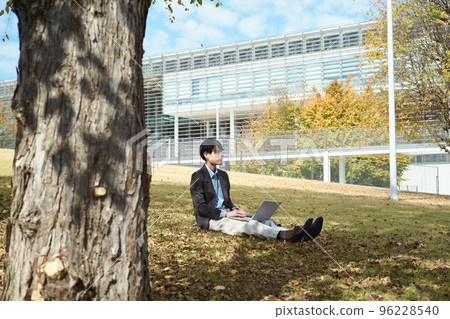 A man sitting on the lawn and using a laptop A man sitting on the lawn and using a laptop 96228540
