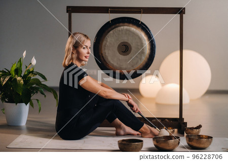 A woman sits with a hammer and next to a gong and Tibetan bowls in the interior A woman sits with a hammer and next to a gong and Tibetan bowls in the interior 96228706