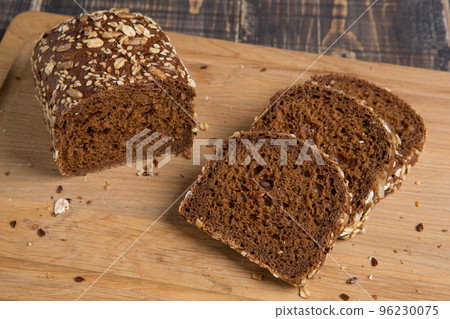 A loaf of rye bread and three sliced pieces, with flax and sunflower seeds, on a cutting board A loaf of rye bread and three sliced pieces, with flax and sunflower seeds, on a cutting board 96230075