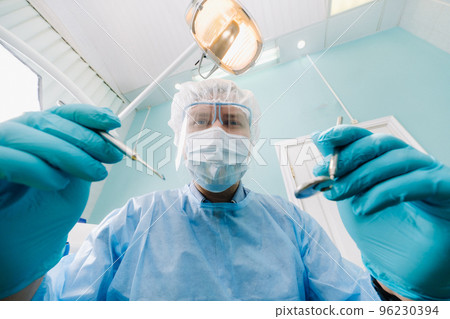 a dentist wearing a protective mask sits nearby and holds instruments in his hands before treating a patient in the dental office 96230394