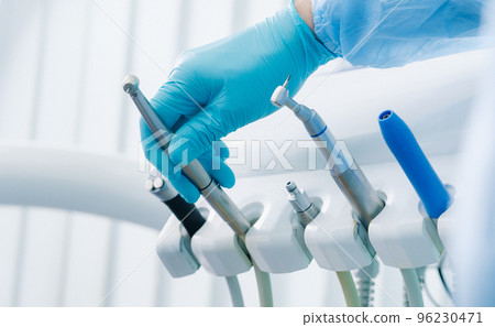 a dentist wearing gloves in the dental office holds a tool before working 96230471