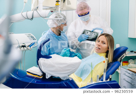 The dentist explains the details of the X-ray to his colleague, the patient is surprised by what is happening 96230559
