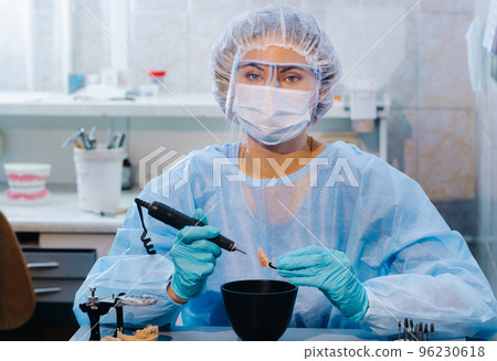 A dental technician in protective clothing is working on a prosthetic tooth in his laboratory 96230618