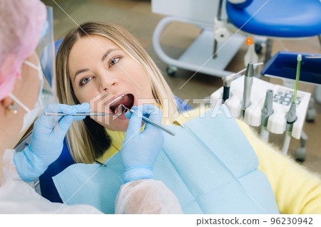 a dentist in a protective mask sits next to him and treats a patient in the dental office a dentist in a protective mask sits next to him and treats a patient in the dental office 96230942