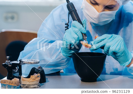 A dental technician in protective clothing is working on a prosthetic tooth in his laboratory 96231129