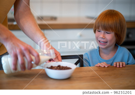Man pouring milk into the plate of his son Man pouring milk into the plate of his son 96231201
