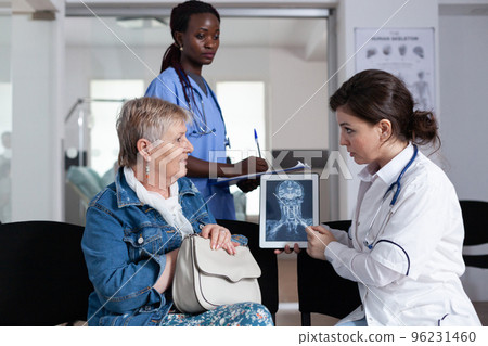 African american nurse making diagnosis notes of elderly woman x ray. Doctor explaining medical condition to old patient in geriatric hospital. Old woman receiving test results in lobby clinic. 96231460