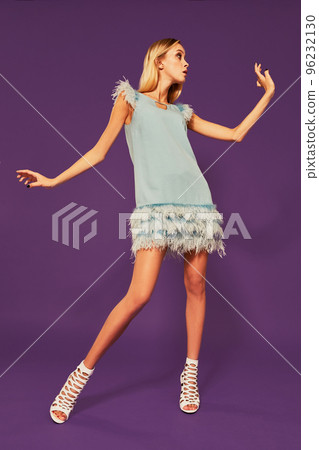 Image of pretty young blonde girl in blue cocktail dress dancing on purple background in studio Image of pretty young blonde girl in blue cocktail dress dancing on purple background in studio 96232130