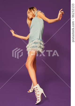 Image of pretty young blonde girl in blue cocktail dress dancing on purple background in studio Image of pretty young blonde girl in blue cocktail dress dancing on purple background in studio 96232133
