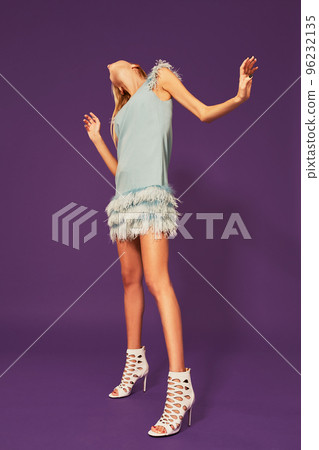 Image of pretty young blonde girl in blue cocktail dress dancing on purple background in studio Image of pretty young blonde girl in blue cocktail dress dancing on purple background in studio 96232135