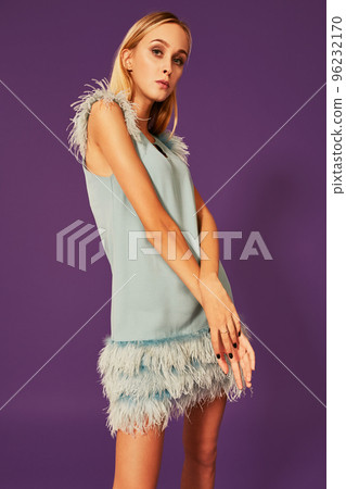Image of cute beautiful slim blonde woman in elegant cocktail blue dress is posing at studio on purple background. Image of cute beautiful slim blonde woman in elegant cocktail blue dress is posing at studio on purple background. 96232170