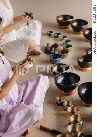Two female yoga teachers play on Tibetan bowls in the gym during a yoga retreat 96233685