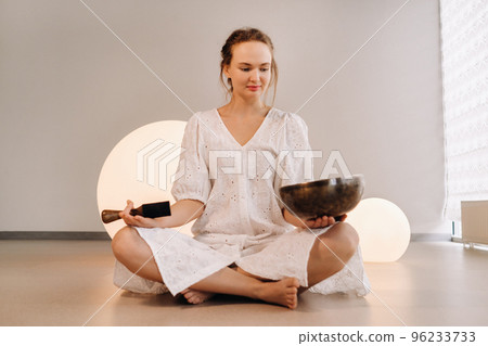 Portrait of a female yoga teacher playing a Tibetan bowl or singing a bell in the gym during a yoga retreat 96233733