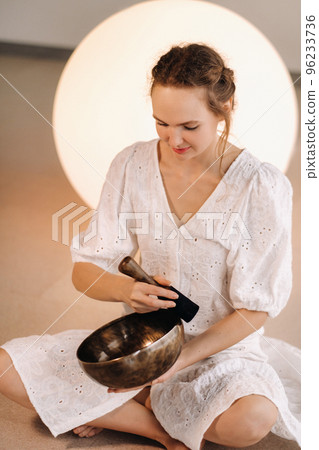 Portrait of a female yoga teacher playing a Tibetan bowl or singing a bell in the gym during a yoga retreat 96233736