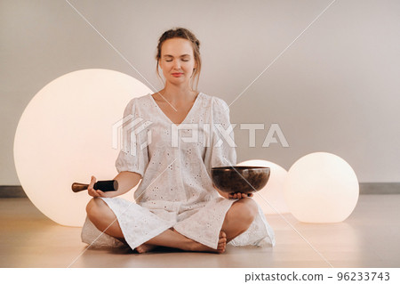 Portrait of a female yoga teacher playing a Tibetan bowl or singing a bell in the gym during a yoga retreat 96233743