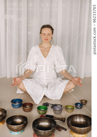 A woman sits with Tibetan bowls in the lotus position before doing yoga in the gym 96233765