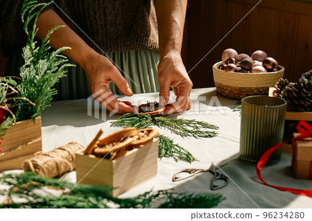 Woman making Christmas arrangement with fir branches and dried oranges. Female hands creating Christmas craft handmade decor. New year celebration. Winter holidays. 96234280