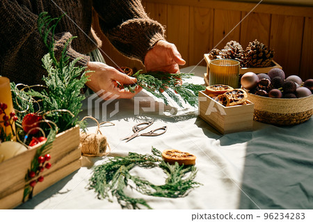 Woman making Christmas arrangement with fir branches and dried oranges. Female hands creating Christmas craft handmade decor. New year celebration. Winter holidays. Woman making Christmas arrangement with fir branches and dried oranges. Female hands creating Christmas craft handmade decor. New year celebration. Winter holidays. 96234283