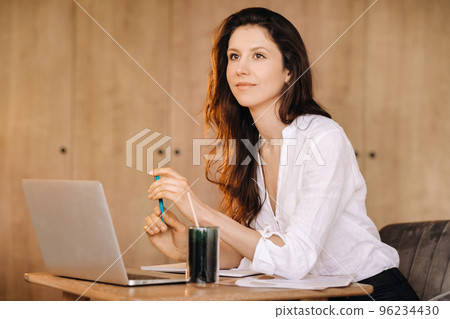 The girl is sitting at a desk in the office and working The girl is sitting at a desk in the office and working 96234430