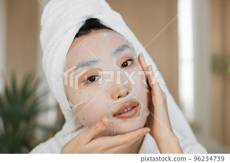 Healthy asian female with cotton mask sheet on face and towel on head over exotic background 96234739