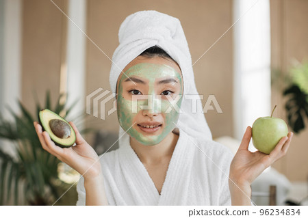 Portrait of beautiful young asian woman with green cosmetic mask apple and avocado in her hands Portrait of beautiful young asian woman with green cosmetic mask apple and avocado in her hands 96234834