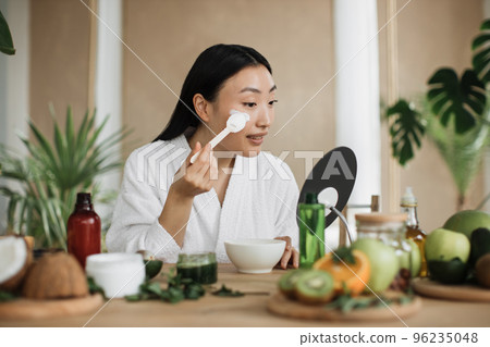 Healthy asian woman sitting preparing cream and applying on face using wooden spoon. 96235048