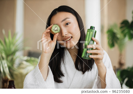 Portrait of beautiful asian girl making nourishing mask with kiwi in tropical exotic studio. 96235080