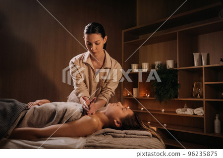 A masseuse gives a body massage to a woman in a spa center. A professional masseur massages the shoulder of a girl lying in a spa center 96235875