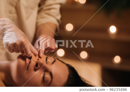 A cosmetologist girl does a facial and neck massage to a girl in the office for skin elasticity 96235896