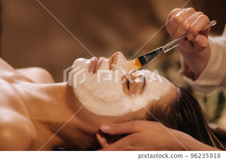A cosmetologist makes a mask for a woman's face to rejuvenate the skin. Cosmetology 96235918
