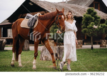 Beautiful girl in a white sundress next to a horse on an old ranch Beautiful girl in a white sundress next to a horse on an old ranch 96236232