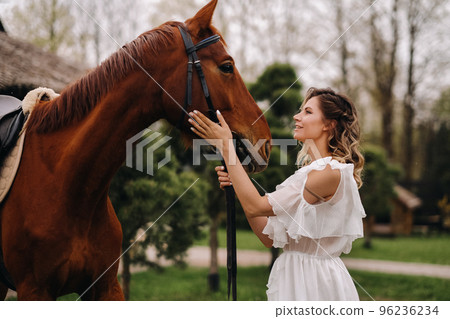 Beautiful girl in a white sundress next to a horse on an old ranch 96236234