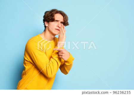 Portrait of young man with curly hair posing, whispering secret information isolated over blue background Portrait of young man with curly hair posing, whispering secret information isolated over blue background 96236235