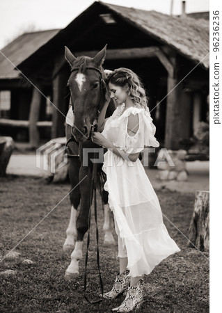 Beautiful girl in a white sundress next to a horse on an old ranch. black and white photo Beautiful girl in a white sundress next to a horse on an old ranch. black and white photo 96236236