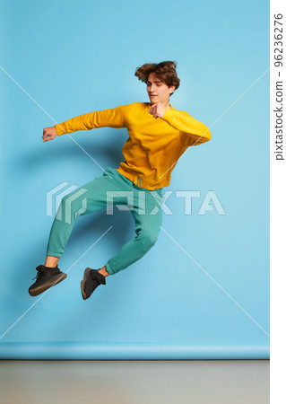 Portrait of young man with curly hair posing in a jump isolated over blue background. Cheerful mood 96236276