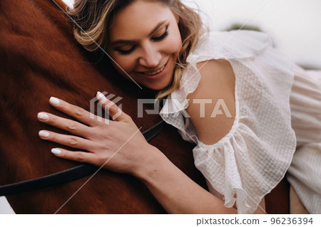 A woman in a white sundress riding a horse near a farm 96236394