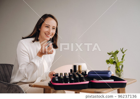 The aromatherapist girl is sitting in her office and holding a bottle of aromatic oils. there are essential oils on the table The aromatherapist girl is sitting in her office and holding a bottle of aromatic oils. there are essential oils on the table 96237136