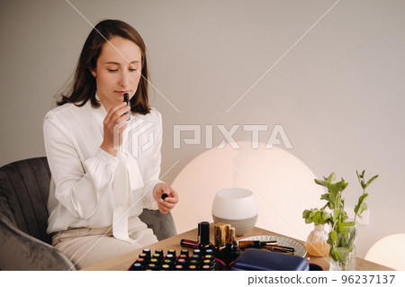 The aromatherapist girl is sitting in her office and holding a bottle of aromatic oils. there are essential oils on the table The aromatherapist girl is sitting in her office and holding a bottle of aromatic oils. there are essential oils on the table 96237137