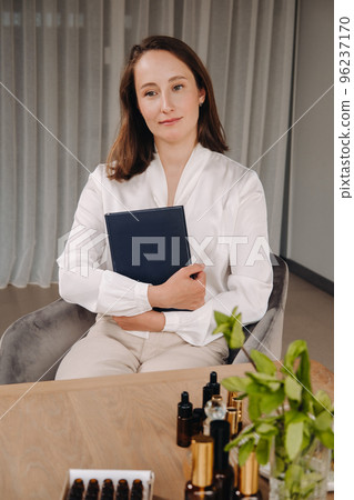 portrait of a smiling girl-woman sitting in an armchair. An aromatherapist in a white blouse is sitting in the office 96237170