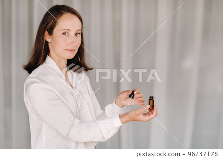 A girl with a white blouse holds essential oils in her hands and drips on her wrist 96237178