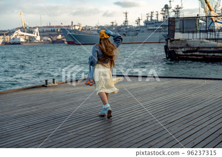 Outdoors fashion portrait of a beautiful middle aged woman walking on the beach. Marine background. Dressed in a stylish warm blue sweater, yellow skirt and beret. Outdoors fashion portrait of a beautiful middle aged woman walking on the beach. Marine background. Dressed in a stylish warm blue sweater, yellow skirt and beret. 96237315