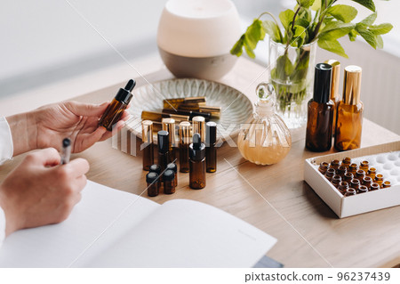 Close-up of female hands holding a bottle of essential oil and writing an entry in a notebook, aromatherapy Close-up of female hands holding a bottle of essential oil and writing an entry in a notebook, aromatherapy 96237439