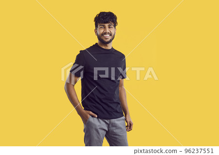 Young South Asian man with dark curly hair posing with smile in casual clothes stands in studio Young South Asian man with dark curly hair posing with smile in casual clothes stands in studio 96237551