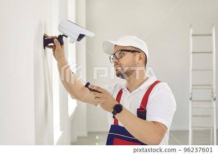 A Caucasian male repairman in uniform and glasses holds a screwdriver and installs video surveillance. 96237601