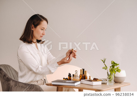 The aromatherapist girl is sitting in her office and holding a bottle of aromatic oils. there are essential oils on the table 96238034
