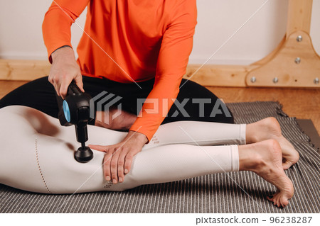 A male masseur massages a girl's body with a percussion massager to prepare for a stretching simulator A male masseur massages a girl's body with a percussion massager to prepare for a stretching simulator 96238287