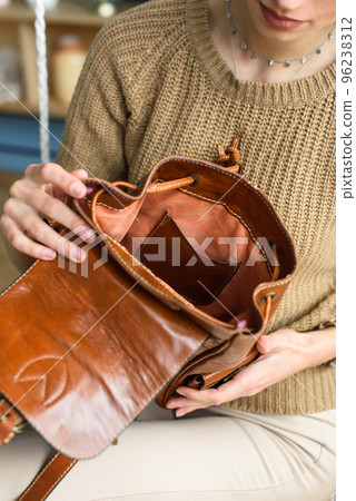 beautiful slender girl in beige pants and olive sweater posing while sitting in a swing chair with a small shiny brown leather backpack 96238312