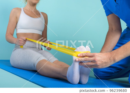 Girl performs exercises with a physiotherapist. Cyan background Girl performs exercises with a physiotherapist. Cyan background 96239680