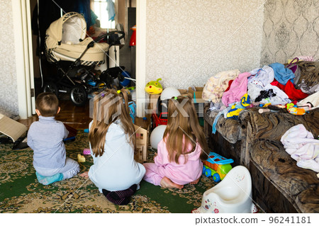 Three unrecognizable children are playing in a dirty cluttered room 96241181