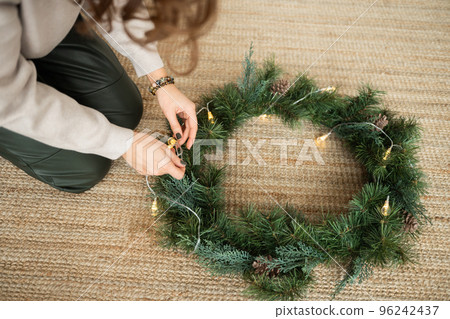 A girl weaves a Christmas wreath from Christmas trees A girl weaves a Christmas wreath from Christmas trees 96242437